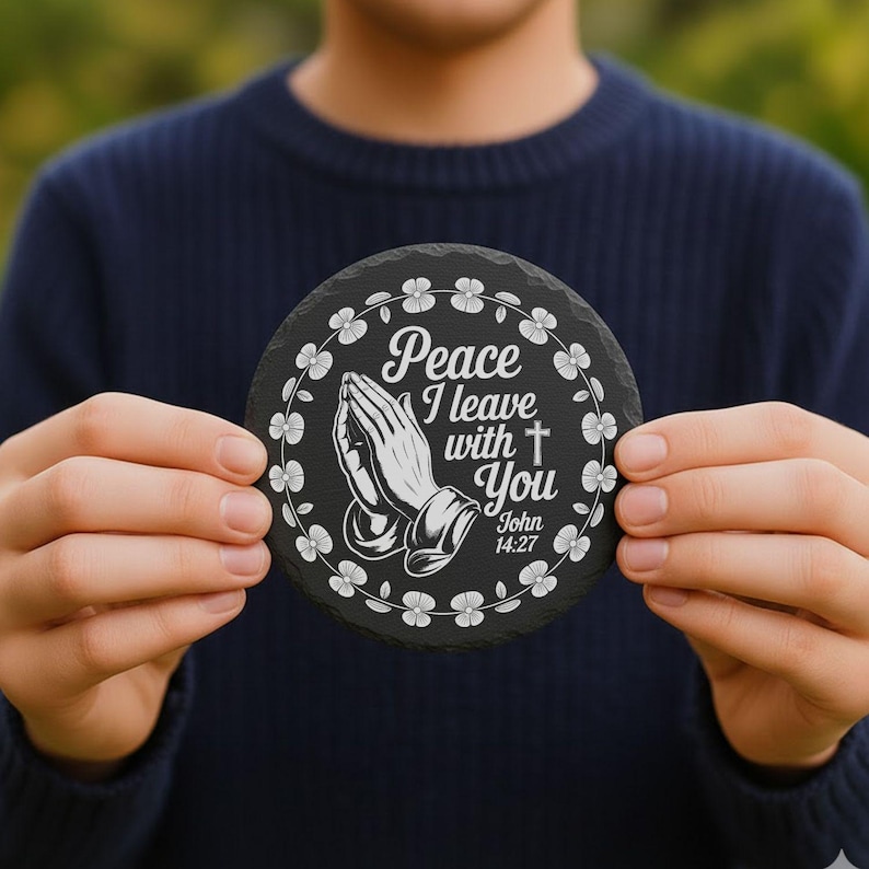 May include: Round black slate coaster with white floral border and text "Peace I leave with You" with praying hands and a cross. The text also includes "John 14:27".
