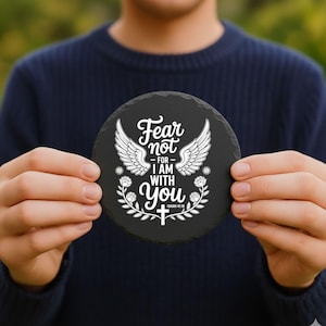 May include: A circular, black slate coaster featuring white text and decorative details. The text says "Fear not - for I am with you" with angel wings and floral designs. A decorative item for the home.