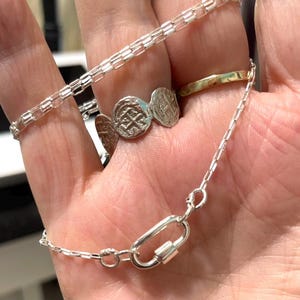 May include: Two silver chains with a silver carabiner clasp. The chain on top is a box chain and the chain on the bottom is a delicate chain.