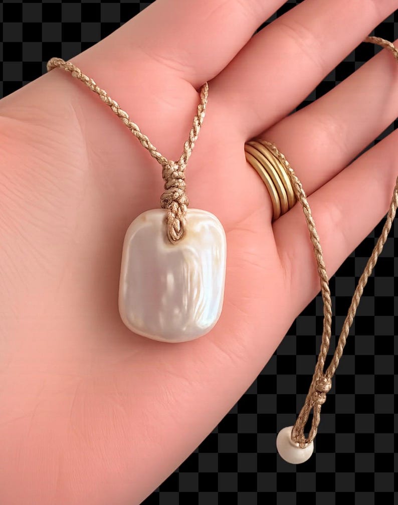 May include: A rectangular, iridescent white pearl pendant suspended from a thin, braided tan cord. The pendant features a smooth, polished surface with a soft lustre. The cord includes a small, round white bead at the end of the adjustable closure.