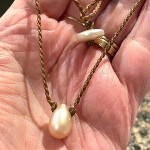 May include: A brown leather cord necklace with a large, teardrop-shaped pearl pendant and a smaller, round pearl charm.