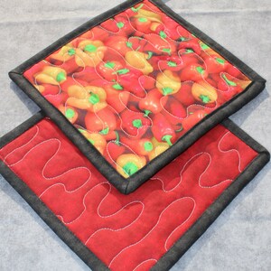 May include: Two quilted pot holders. One is red with a wavy pattern and the other has a pattern of red and yellow peppers.