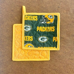 May include: Two green and yellow quilted pot holders with the Green Bay Packers logo and the word "Packers" on them.