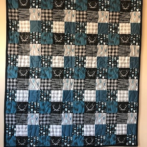 May include: A blue, black, and white patchwork quilt with a variety of patterns, including deer, arrows, and plaid. The quilt is quilted with a diamond pattern.