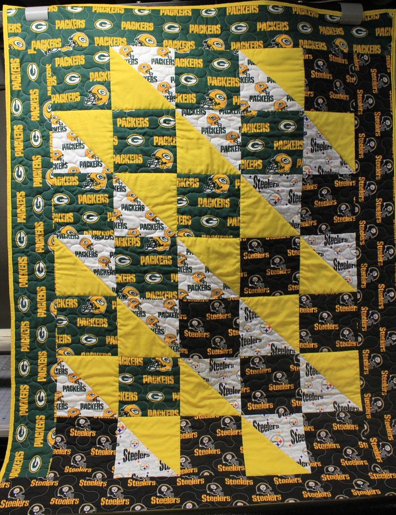 May include: A green and yellow patchwork quilt with the Green Bay Packers and Pittsburgh Steelers logos. The quilt is made of squares and triangles.