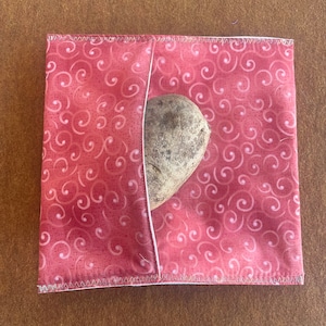 May include: A red fabric pouch with a white trim and a swirl pattern. A brown potato is inside the pouch.