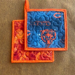 May include: A set of two quilted pot holders. One is blue with a Chicago Bears logo and the other is orange with a swirl pattern.