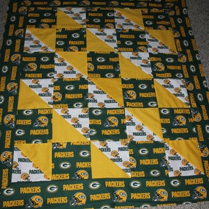 May include: A green and yellow patchwork quilt with the word "Packers" repeated throughout. The quilt is made up of squares and triangles.