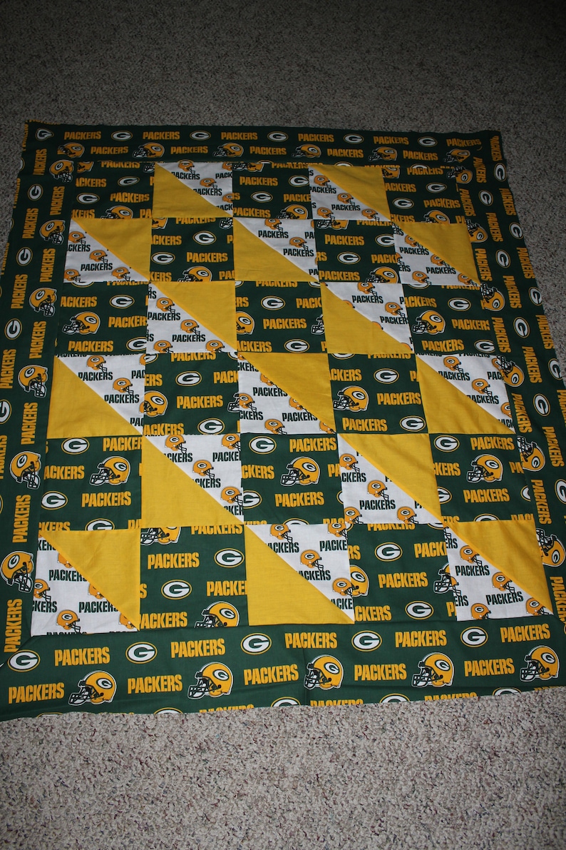 May include: A green and yellow patchwork quilt with the word "Packers" repeated throughout. The quilt is made up of squares and triangles.
