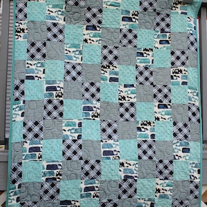May include: A blue and white patchwork quilt with a whale pattern. The quilt is made of various fabrics, including stripes, plaid, and solid colors.