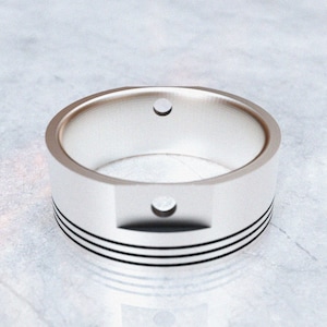 May include: A silver-colored ring with a cylindrical design, featuring two small circular holes and three black horizontal lines. The ring has a unique, industrial aesthetic.