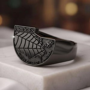 May include: A black ring with a detailed map of the United States. The ring features the word "BRIDGES" at the top and "UNITED CITIES OF AMERICA" at the bottom. The ring is set on a white surface.
