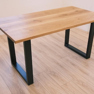 Könnte beinhalten: Ein rechteckiger Holztisch mit einer hellbraunen Tischplatte und schwarzen Metallbeinen. Der Tisch ist etwa 122 cm lang und 61 cm breit, mit einer Höhe von etwa 76 cm. Die Beine haben ein schlichtes, modernes Design.