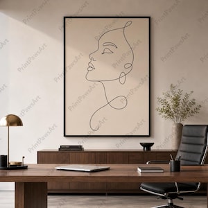 May include: A framed minimalist art print showing a continuous line drawing of a woman's profile in black against a beige background. The artwork is displayed in a modern office setting with a wooden desk, black chair, and a gold desk lamp.
