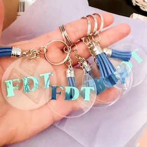 May include: Five clear acrylic keychains with silver rings and blue tassels. Each keychain has the letters "FDT" in teal lettering.