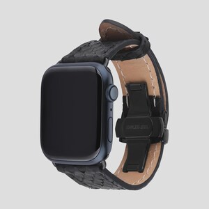 May include: A black smartwatch with a textured black leather band. The watch has a dark blue face and a black stainless steel clasp. The band is secured with a black clasp that reads "STAINLESS STEEL".