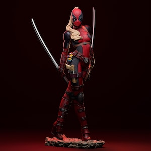 Puede incluir: Figura detallada de una superheroína con un traje rojo y negro, máscara y pelo rubio, sosteniendo dos katanas. La figura tiene un cinturón de herramientas con una pistola y otros accesorios. La base es una superficie rocosa texturizada. El fondo es rojo oscuro.