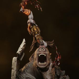 May include: A detailed statue depicting a muscular figure in golden armor, wielding a fiery weapon, attacking a cyclops. The cyclops has a wide open mouth and a single eye. The statue is set against a dark background.
