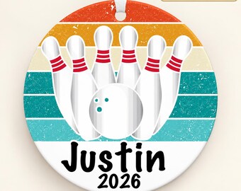 May include: A round ceramic ornament featuring a bowling theme with six white pins and a bowling ball. The background has horizontal stripes in orange, yellow, and teal. The text "Justin" and "2026" is printed in black at the bottom.