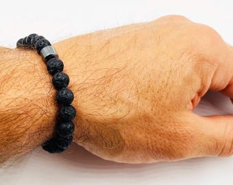May include: A black lava rock bracelet with a silver bead accent. The bracelet is worn on a person's wrist.