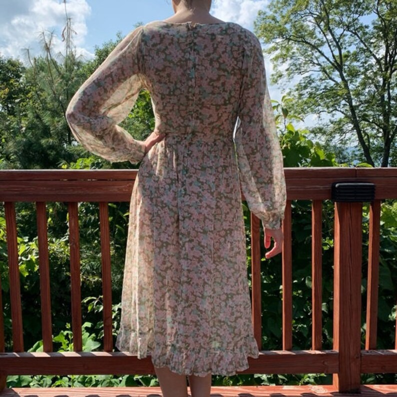 May include: A long-sleeved, floral print dress with a V-neckline and a gathered skirt. The dress is made of a sheer fabric and has a light pink and green color scheme.