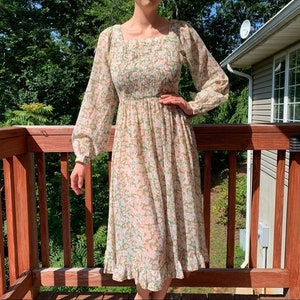 May include: A long-sleeved, floral print dress with a square neckline and a gathered waist. The dress has a ruffled hem and is made of a lightweight fabric.