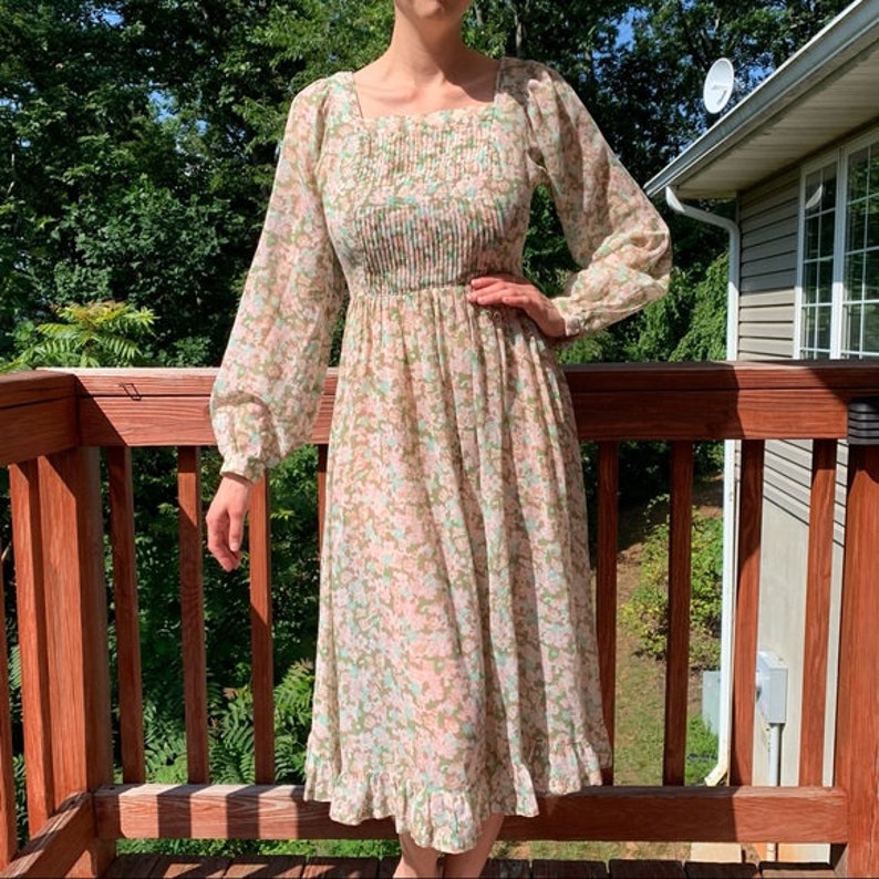 May include: A long-sleeved, floral print dress with a square neckline and a gathered waist. The dress has a ruffled hem and is made of a lightweight fabric.