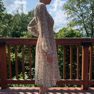 May include: A long-sleeved floral dress with a V-neckline and a ruffled hem. The dress is made of a sheer fabric and has a light pink and green floral pattern.