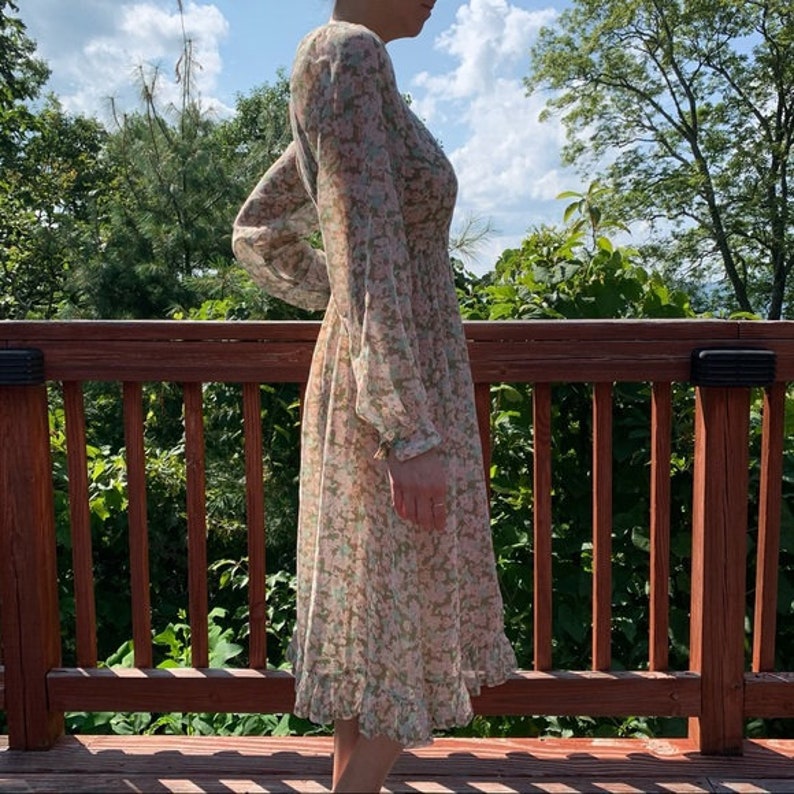 May include: A long-sleeved floral dress with a V-neckline and a ruffled hem. The dress is made of a sheer fabric and has a light pink and green floral pattern.