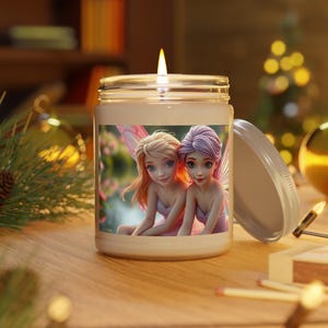 May include: A lit candle in a glass jar with a metal lid. The jar features a colorful image of two fairies with pink wings and dresses. The candle sits on a wooden surface.