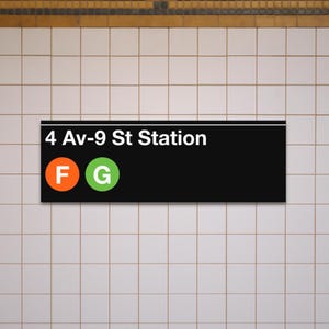 May include: A black rectangular sign with white text reading "4 Av-9 St Station." Below the text are two circles, one orange with the letter "F" and one green with the letter "G." The sign is mounted on a tiled wall.