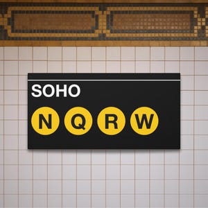 May include: A black rectangular sign with the word "SOHO" in white letters above four yellow circles with the letters "N", "Q", "R", and "W". The sign is mounted on a white tiled wall.