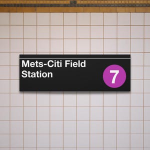 May include: A black sign displaying "Mets-Citi Field Station" in white text, with a purple circle containing the number "7". The sign is fixed to a tiled wall.
