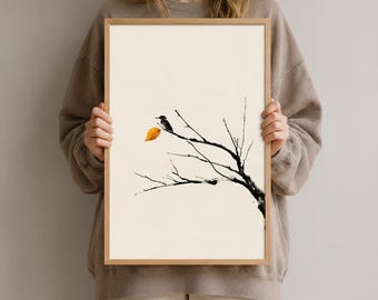 Könnte beinhalten: Ein gerahmter vertikaler Kunstdruck mit einer minimalistischen schwarzen Tuschezeichnung eines kleinen Vogels, der auf einem kahlen Ast mit einem einzelnen leuchtend orangefarbenen Blatt sitzt, vor einem cremefarbenen Hintergrund in einem hellen Holzrahmen.