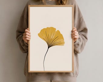 Könnte beinhalten: Ein rechteckiger gerahmter Kunstdruck mit einer einzelnen senfgelben Ginkgo-Blatt-Illustration, die auf einem hellen cremefarbenen Hintergrund zentriert ist. Das Blatt hat feine schwarze Adern, die vom Stiel in die fächerförmige Struktur verlaufen.