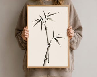Könnte beinhalten: Ein gerahmter vertikaler Wandkunstdruck mit einer schwarzen Tuschezeichnung eines Bambusstängels mit schmalen Blättern auf einem cremefarbenen Hintergrund. Das Kunstwerk ist in einem hellen Holzrahmen mit einem schlichten Rand eingefasst.