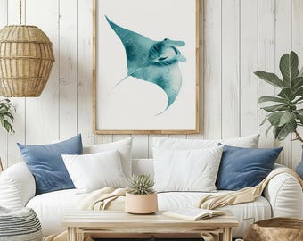 May include: A framed art print featuring a teal manta ray illustration. The artwork is set against a white background, framed in natural wood, and hangs above a white sofa with blue and white pillows. The room has a coastal theme.
