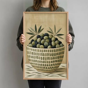 May include: A framed wall art print featuring a bowl filled with green and black olives. The bowl has a textured grid pattern in shades of green and beige. Two olive branches with pointed leaves extend from the top of the olive pile.