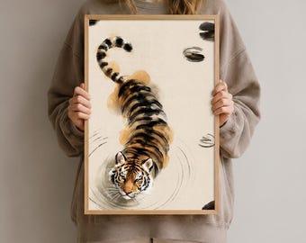 Könnte beinhalten: Ein gerahmter Kunstdruck, der einen Tiger beim Schwimmen im Wasser zeigt. Der Tiger hat orangefarbene und schwarze Streifen und ist von oben dargestellt, wobei er Wellen im Wasser erzeugt. Der Hintergrund ist cremefarben mit dunklen Formen.