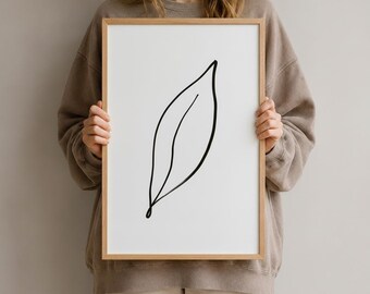 Könnte beinhalten: Ein gerahmter Kunstdruck mit einer einzelnen schwarzen Strichzeichnung eines Blattes, zentriert auf weißem Hintergrund. Das Kunstwerk befindet sich in einem hellen Holzrahmen mit schlichtem, sauberem Rand und zeigt eine klare botanische Darstellung.