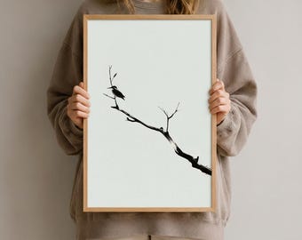 Könnte beinhalten: Ein gerahmter vertikaler Wandkunstdruck mit einer minimalistischen schwarzen Tuschezeichnung eines einzelnen Vogels, der auf einem kahlen, dünnen Ast vor einem cremeweißen Hintergrund sitzt. Der Rahmen besteht aus hellem Holz.