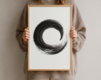Könnte beinhalten: Ein rechteckiger Wandkunstdruck in einem hellen Holzrahmen mit einem schwarzen Pinselstrich-Kreis auf weißem Hintergrund. Das kreisförmige Design zeigt sichtbare, texturierte Pinselspuren und ein spitz zulaufendes Ende im vertikalen Rahmen.