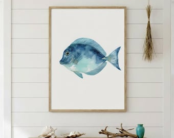 May include: A framed watercolor print of a blue fish. The fish has a light blue body with darker blue accents and a detailed fin. The artwork is displayed on a white wall above a wooden console table.