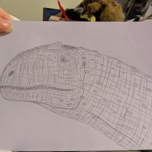 May include: A detailed pencil drawing of a dinosaur's head and neck. The drawing is done in shades of grey on a light purple background.