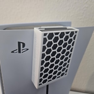 May include: A white PlayStation 5 console with a black honeycomb-shaped air filter attached to the side.