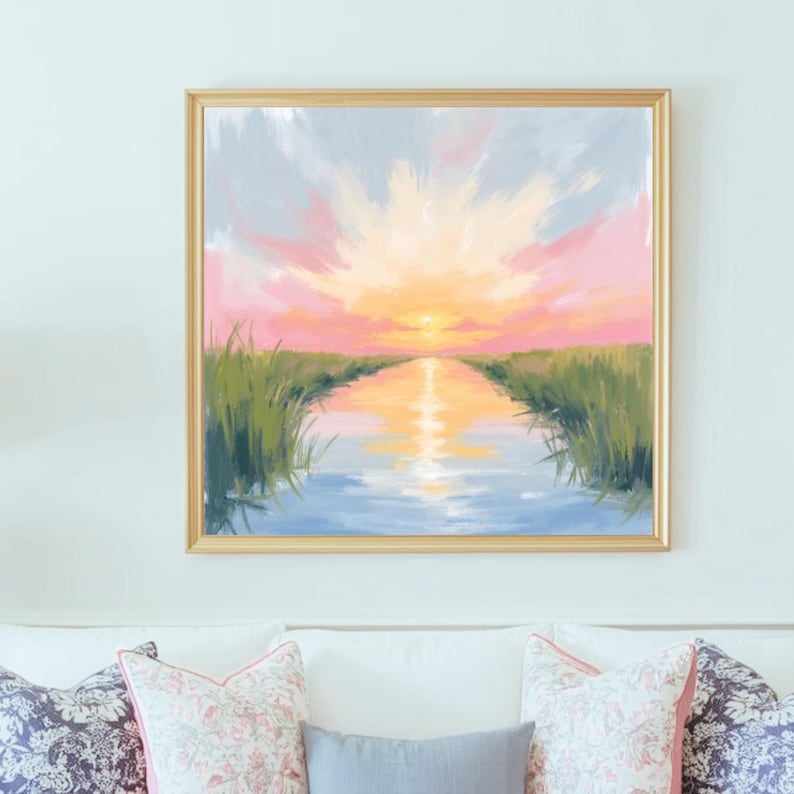 May include: A framed landscape painting depicts a sunset over a waterway. The sky transitions from pink to yellow, reflecting in the water. Green reeds line the banks. The painting is in a gold frame, creating a serene and natural scene.