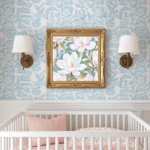 K&ouml;nnte beinhalten: Ein gerahmtes Blumenbild mit wei&szlig;en und rosa Magnolienbl&uuml;ten h&auml;ngt &uuml;ber einem wei&szlig;en Kinderbett. Das Gem&auml;lde hat einen goldenen, verzierten Rahmen. Zwei wei&szlig;e Lampen mit plissierten Schirmen sind an der hellblauen Blumentapete angebracht.