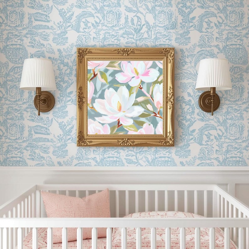 K&ouml;nnte beinhalten: Ein gerahmtes Blumenbild mit wei&szlig;en und rosa Magnolienbl&uuml;ten h&auml;ngt &uuml;ber einem wei&szlig;en Kinderbett. Das Gem&auml;lde hat einen goldenen, verzierten Rahmen. Zwei wei&szlig;e Lampen mit plissierten Schirmen sind an der hellblauen Blumentapete angebracht.