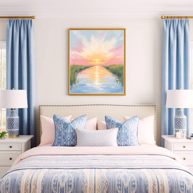 May include: A bedroom scene featuring a bed with a blue and white patterned comforter and decorative pillows. A framed landscape painting with a sunset scene hangs above the bed. Blue curtains and matching lamps complete the decor.