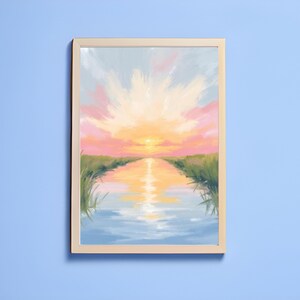 May include: A framed landscape painting depicts a sunset over a body of water. The sky transitions from pink to yellow, with reflections in the water. Green grass lines the water's edge, creating a serene and colorful scene.